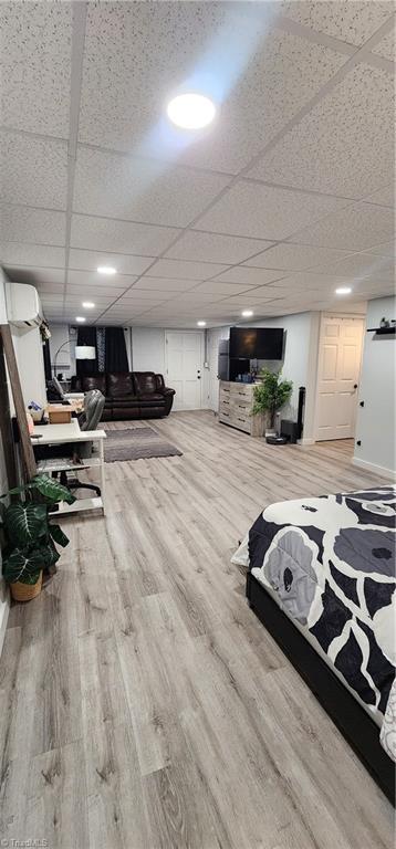 interior space featuring wood finished floors, a drop ceiling, and a wall mounted air conditioner