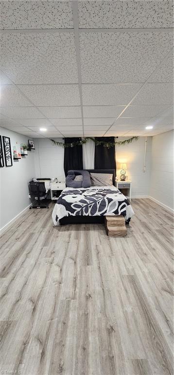 bedroom featuring wood finished floors, baseboards, and a drop ceiling