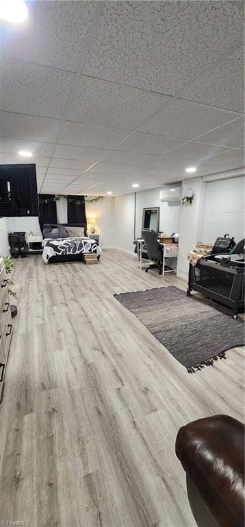 living area featuring a paneled ceiling, wood finished floors, and an AC wall unit