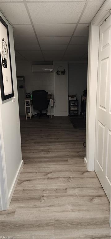 hallway with a paneled ceiling, baseboards, light wood-type flooring, and a wall unit AC