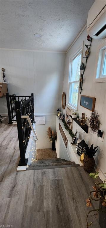 staircase featuring a wall mounted AC, wood finished floors, a textured ceiling, and crown molding