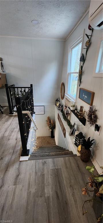 interior space with wood finished floors, an AC wall unit, a textured ceiling, and crown molding
