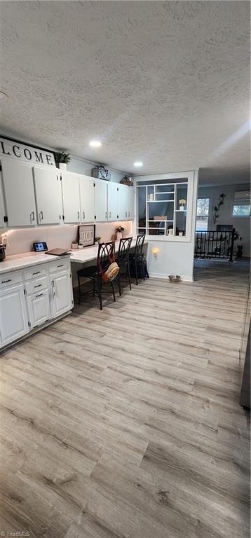 interior space with white cabinets, a textured ceiling, and light wood finished floors