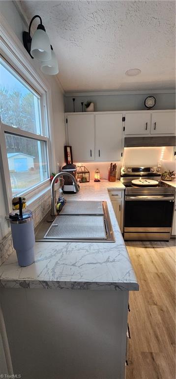 kitchen featuring stainless steel range with electric cooktop, white cabinetry, a sink, and a textured ceiling