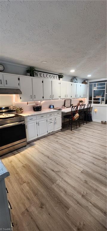 kitchen with a textured ceiling, light wood-style flooring, light countertops, electric range, and white cabinets