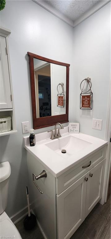 half bath featuring wood finished floors, a textured ceiling, vanity, baseboards, and toilet