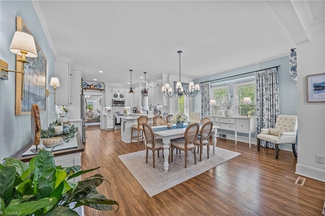 dining space with crown molding, visible vents, dark wood finished floors, and a chandelier
