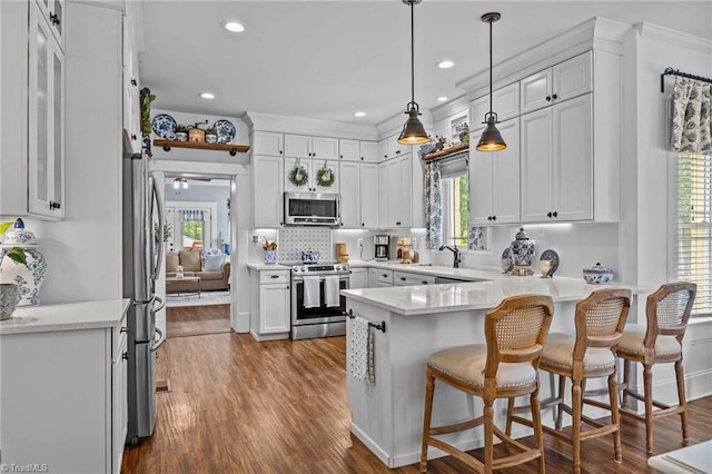 kitchen with white cabinets, a sink, stainless steel appliances, a peninsula, and dark wood-style floors