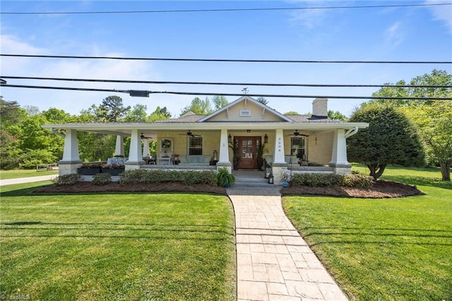 view of front of home with ceiling fan, a front yard, covered porch, and a chimney