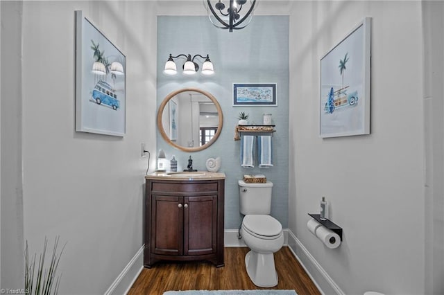 bathroom with wood finished floors, vanity, baseboards, toilet, and an inviting chandelier