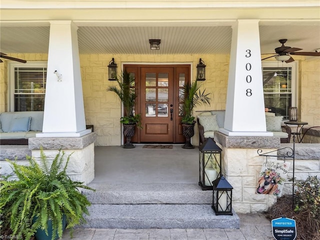 view of exterior entry with covered porch, a ceiling fan, and stone siding
