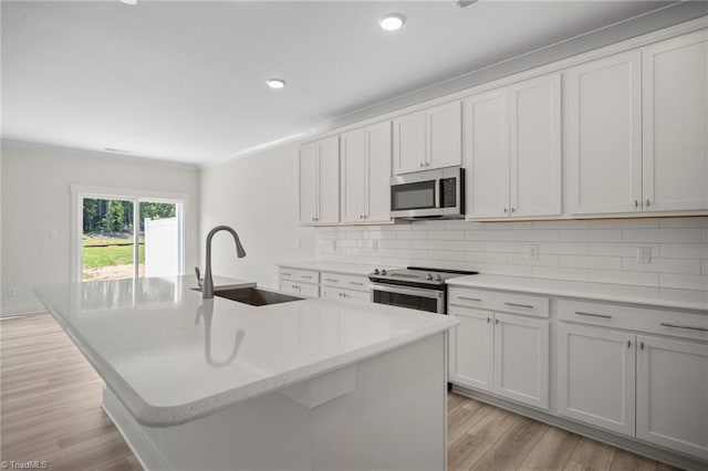 kitchen with light wood-type flooring, appliances with stainless steel finishes, an island with sink, backsplash, and sink