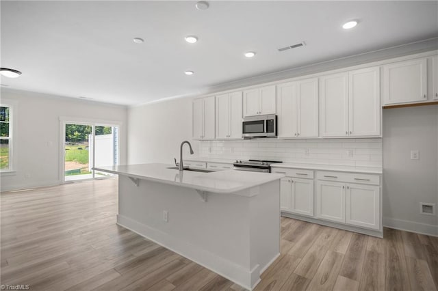 kitchen with a kitchen island with sink, light hardwood / wood-style floors, backsplash, stainless steel appliances, and sink