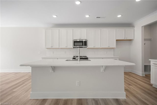 kitchen with a kitchen island with sink, appliances with stainless steel finishes, a kitchen bar, tasteful backsplash, and light hardwood / wood-style floors