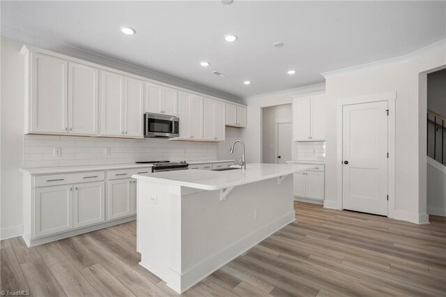 kitchen with appliances with stainless steel finishes, an island with sink, tasteful backsplash, white cabinetry, and light hardwood / wood-style floors