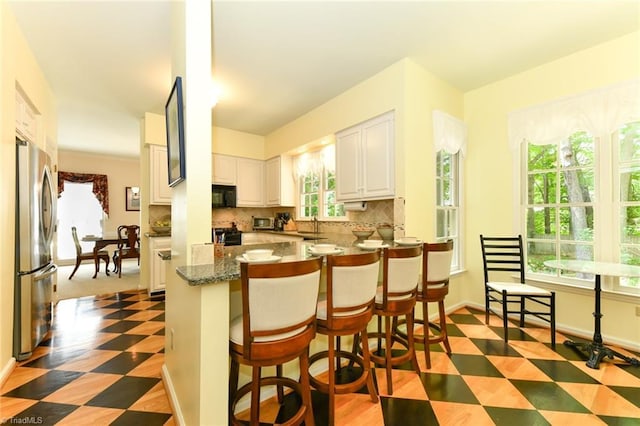 kitchen with freestanding refrigerator, black microwave, light floors, white cabinetry, and backsplash