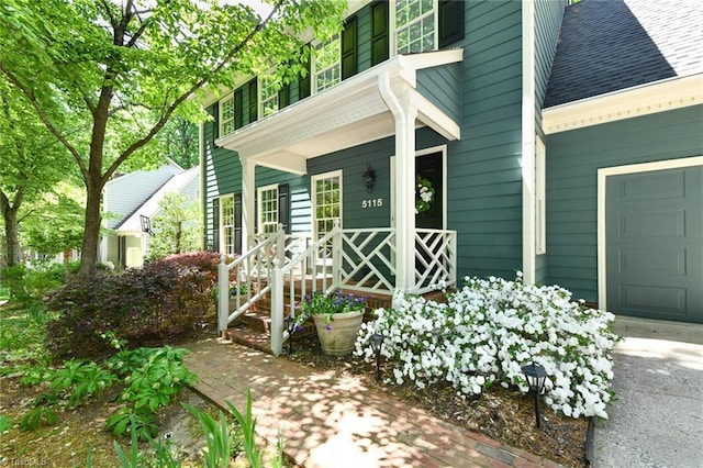 view of exterior entry featuring covered porch, roof with shingles, and a garage