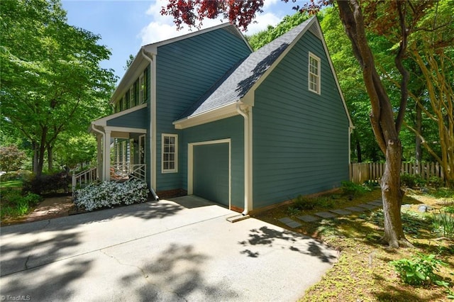 view of side of home featuring a garage, fence, a shingled roof, a porch, and driveway