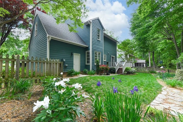 view of home's exterior with a lawn, fence, a wooden deck, and roof with shingles