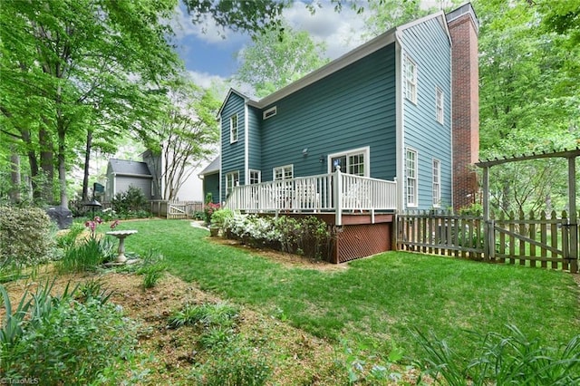 back of property with a lawn, a wooden deck, a chimney, and a fenced backyard