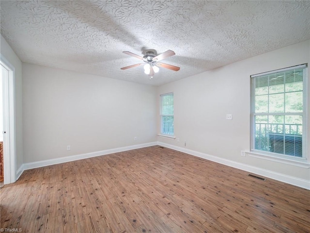 empty room featuring ceiling fan, a healthy amount of sunlight, wood-type flooring, and a textured ceiling