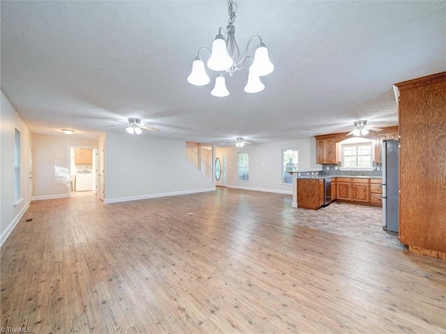 unfurnished living room with a textured ceiling, washer / clothes dryer, light hardwood / wood-style flooring, and a notable chandelier