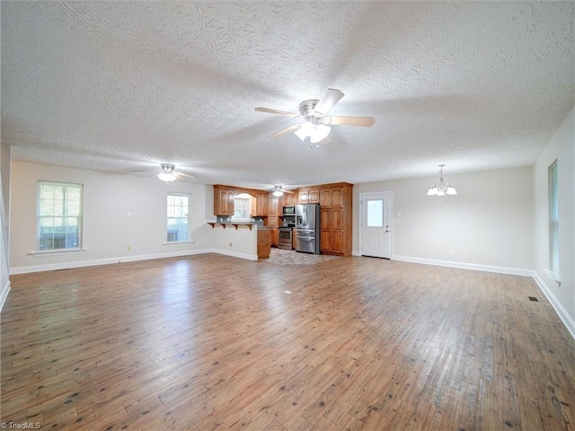 unfurnished living room with ceiling fan with notable chandelier, dark wood-type flooring, and a textured ceiling