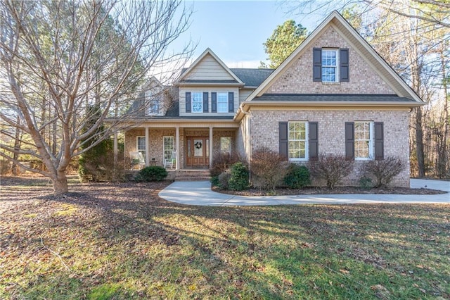 traditional home featuring covered porch, a front lawn, and brick siding