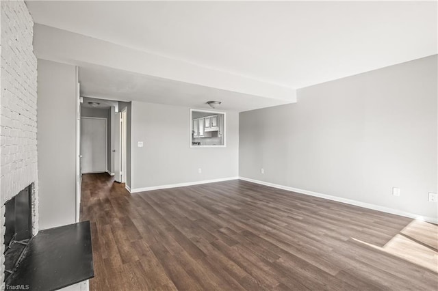 unfurnished living room featuring dark wood-style flooring, a brick fireplace, and baseboards