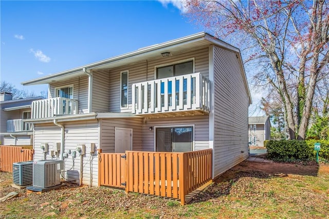 rear view of property featuring cooling unit, a balcony, and fence