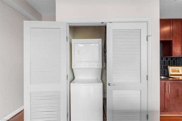 laundry room featuring wood-type flooring and stacked washer and dryer