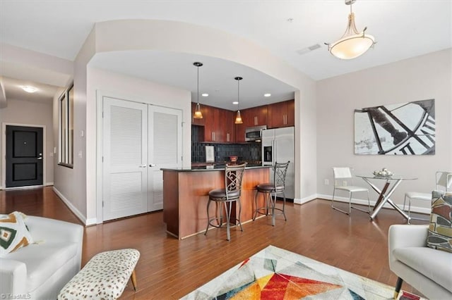 kitchen featuring dark hardwood / wood-style flooring, stainless steel appliances, hanging light fixtures, and a breakfast bar area