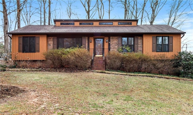 view of front of house featuring brick siding, a shingled roof, and a front yard