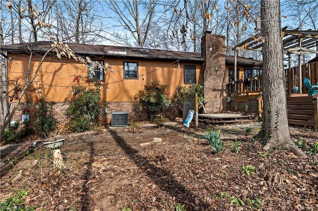 rear view of house with brick siding, a chimney, central AC, and a wooden deck