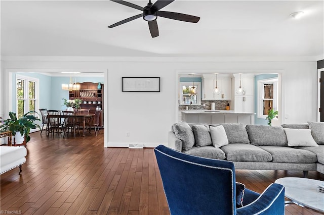 living room featuring ceiling fan with notable chandelier, crown molding, baseboards, and dark wood-style flooring