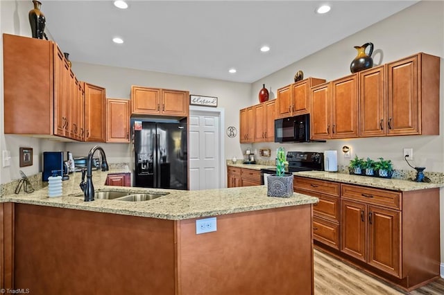 kitchen with sink, light stone counters, black appliances, light hardwood / wood-style floors, and kitchen peninsula