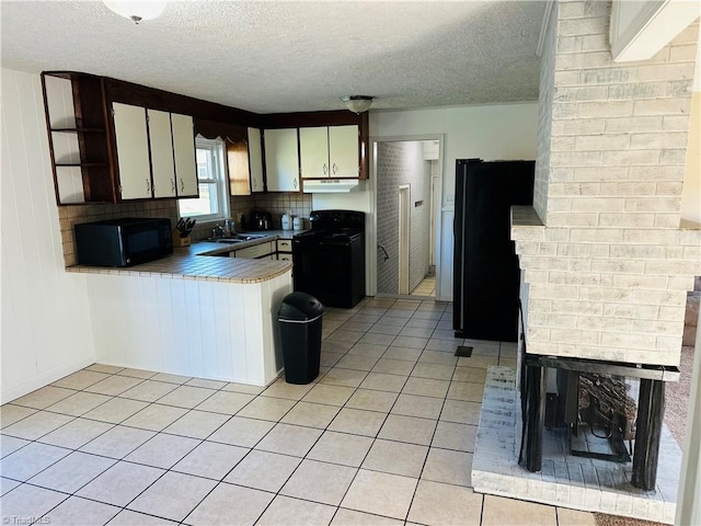 kitchen featuring light tile patterned floors, a peninsula, black appliances, under cabinet range hood, and a sink