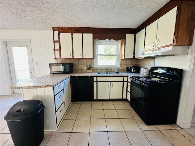 kitchen with a peninsula, light countertops, black appliances, under cabinet range hood, and a sink