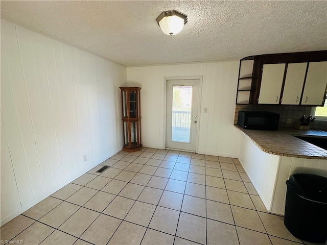 interior space with black microwave, white cabinetry, light tile patterned flooring, and a textured ceiling