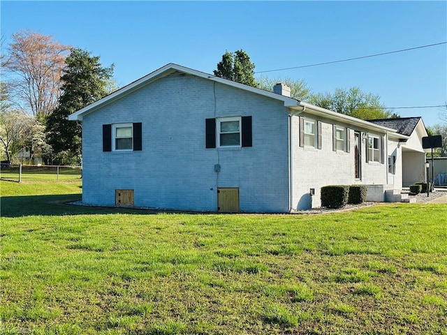 view of property exterior featuring fence, brick siding, a chimney, and a lawn
