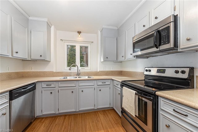 kitchen with a sink, appliances with stainless steel finishes, ornamental molding, and light wood finished floors