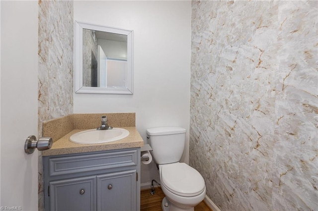 half bathroom with baseboards, toilet, and vanity