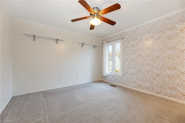 carpeted spare room with ceiling fan, visible vents, baseboards, and ornamental molding