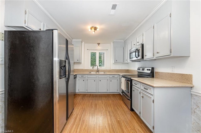 kitchen with visible vents, ornamental molding, a sink, light wood-style floors, and appliances with stainless steel finishes