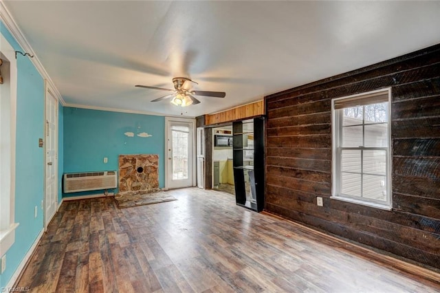 unfurnished living room with a wall mounted air conditioner, wooden walls, ceiling fan, ornamental molding, and wood-type flooring