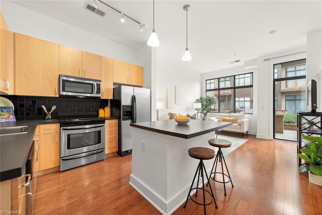 kitchen featuring appliances with stainless steel finishes, light brown cabinetry, decorative light fixtures, and light hardwood / wood-style flooring