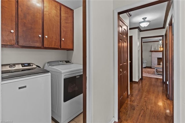 washroom featuring crown molding, dark wood-type flooring, cabinets, washer and dryer, and a brick fireplace