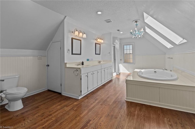 bathroom featuring lofted ceiling with skylight, hardwood / wood-style floors, vanity, a bath, and a textured ceiling