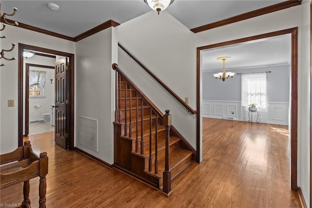 staircase with crown molding, wood-type flooring, and a chandelier