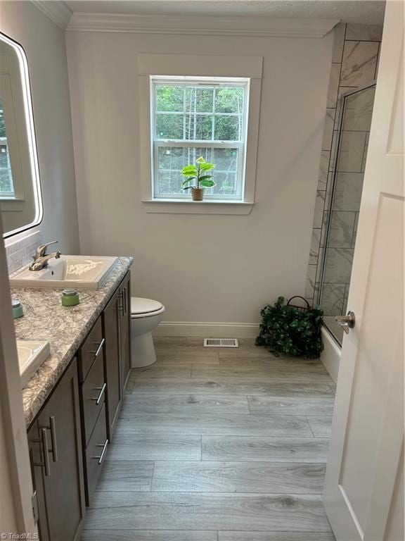 full bathroom featuring crown molding, hardwood / wood-style floors, combined bath / shower with glass door, toilet, and vanity